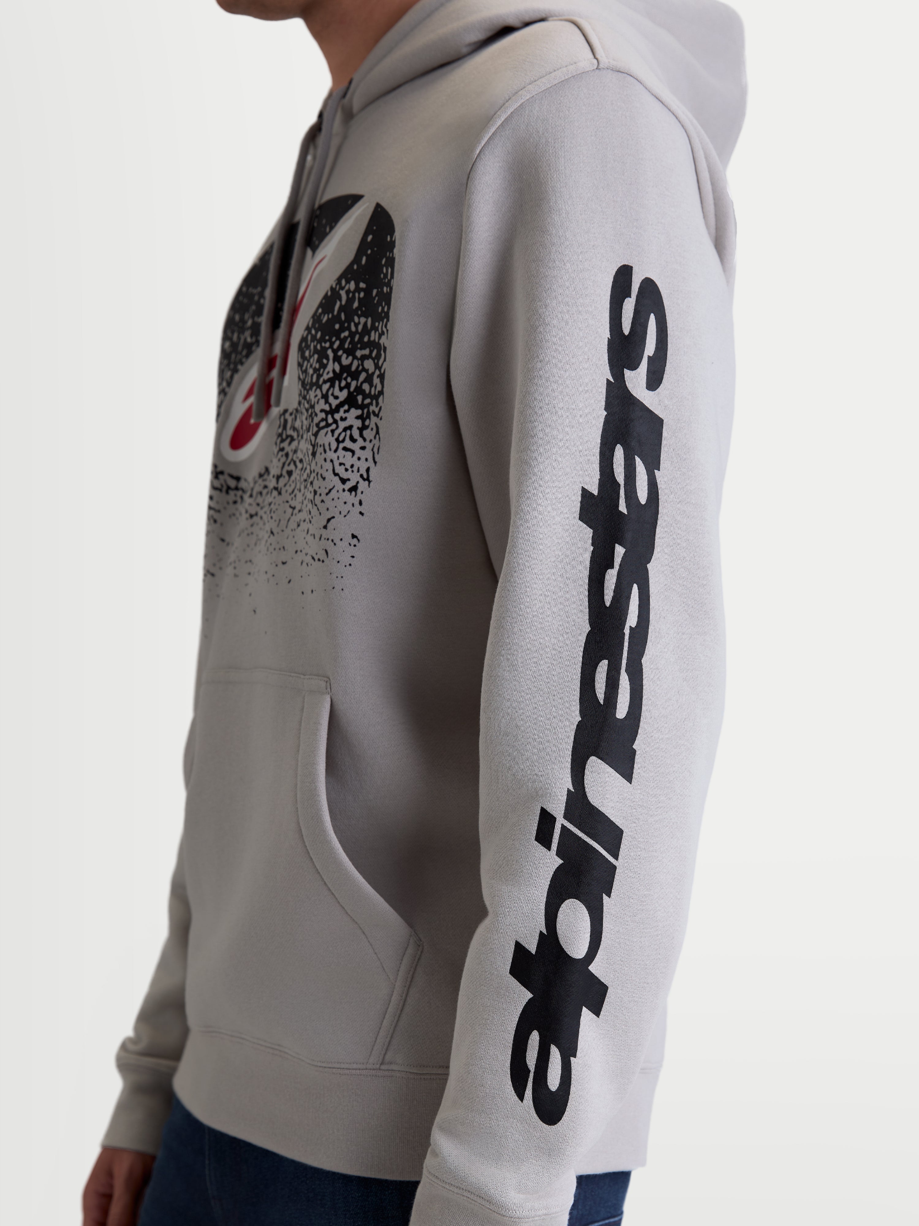 Alpinestars sudadera con capucha Obsessed, sudadera de motorsport casual, unisex, gris y negra, vista lateral en modelo que destaca el logotipo vertical en la manga y el gráfico degradado inspirado en MX en el pecho, confeccionada en algodón y poliéster reciclado.