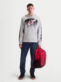 Alpinestars Sudadera con capucha Obsessed, sudadera deportiva para hombre, gris cemento con gráficos degradados en rojo y negro inspirados en el motocross, logotipos en las mangas, mostrada en un modelo con mochila roja