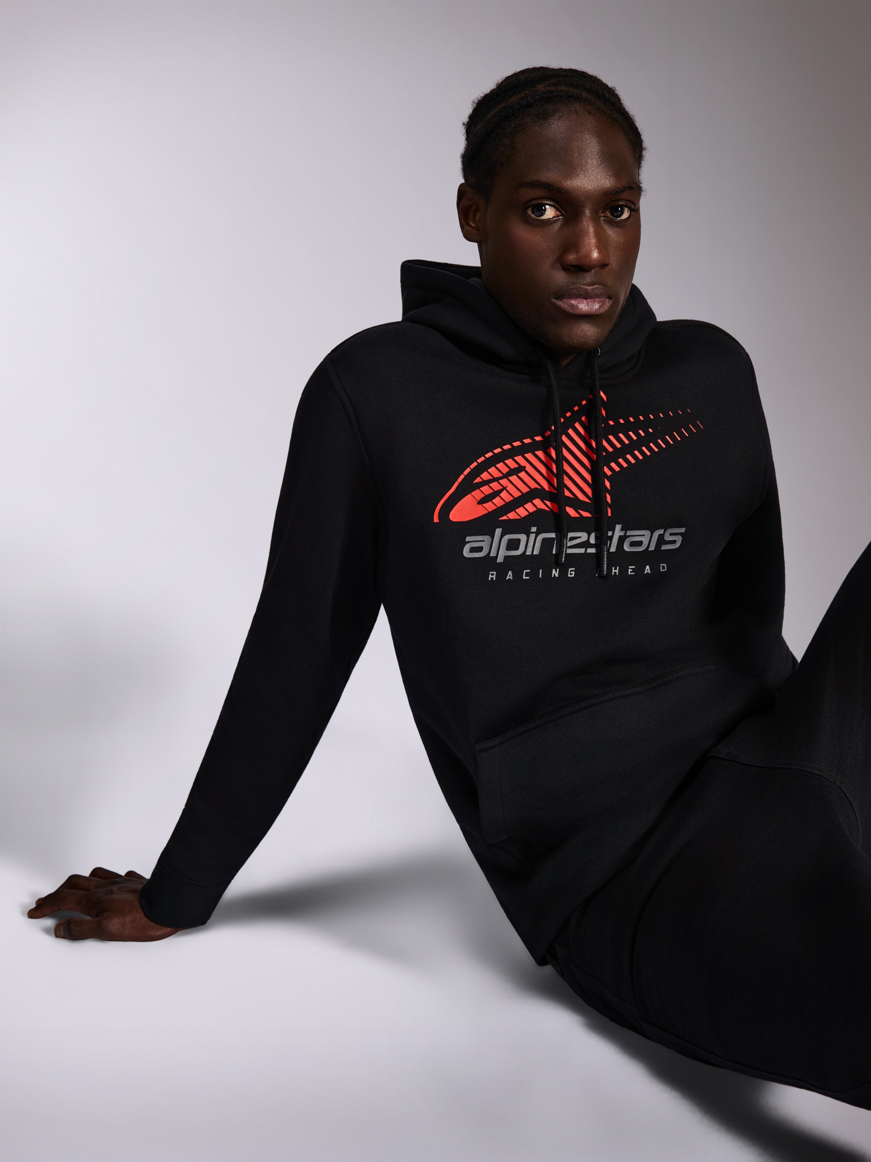 Sudadera con capucha Alpinestars Pulse, negra, ropa urbana informal lucida por un modelo, con logotipo Astars en rojo con efecto de líneas de velocidad y texto 'alpinestars RACING AHEAD' en el pecho, capucha con cordón, manga larga, diseño moderno inspirado en el automovilismo