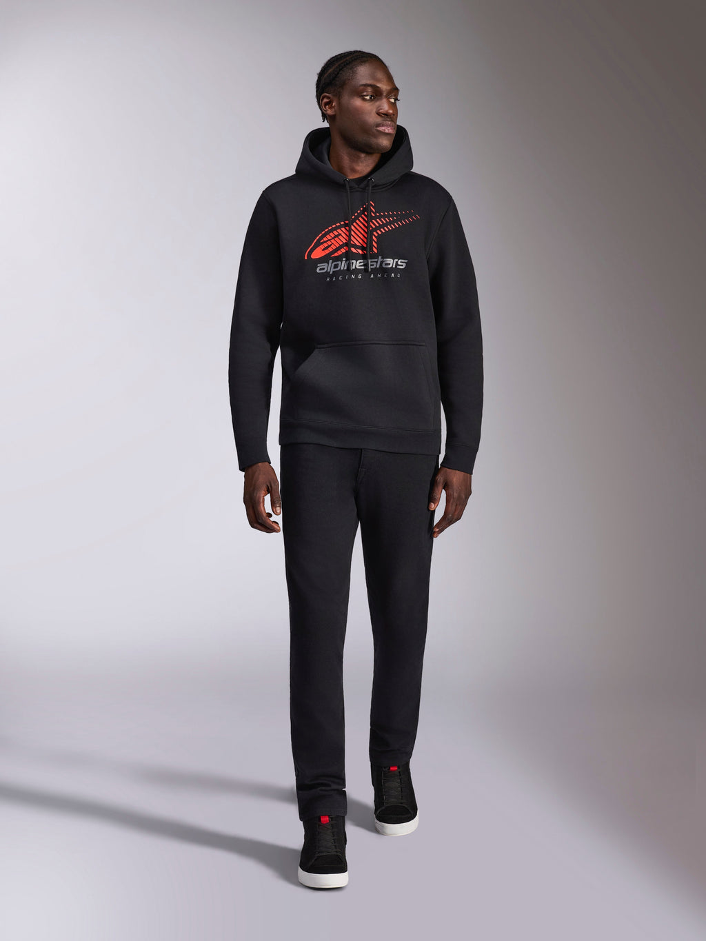 Alpinestars Pulse Hoodie, sudadera urbana casual negra, logotipo Astars Combo en rojo y gris con líneas de velocidad desvanecidas en el pecho, capucha con cordón, bolsillo tipo canguro, manga larga, combinada con pantalones negros y zapatillas, diseño inspirado en el automovilismo