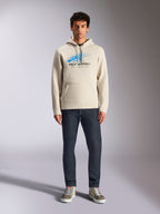 Alpinestars Pulse Hoodie, Off White, sudadera de manga larga con capucha y cordón, logotipo Astars Combo en azul y negro con líneas de velocidad desvanecidas, combinada con vaqueros oscuros y zapatillas, estilo casual motorsport streetwear