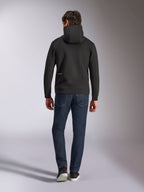 Alpinestars Cypher Hoodie, sudadera de forro polar negro de doble cara, vista posterior con un pequeño logotipo blanco de Alpinestars en la cadera izquierda, capucha de cuello alto, combinada con vaqueros azul oscuro, estilo casual inspirado en el automovilismo