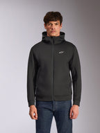 Sudadera con capucha Alpinestars Cypher, sudadera de forro polar negra con cremallera frontal, con capucha de cuello alto con marca blanca y un pequeño logo Astars blanco en el pecho, usada por un modelo con vaqueros azules, ropa urbana casual inspirada en el motorsport.