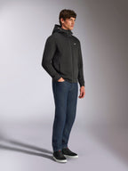 Sudadera con capucha Alpinestars Cypher, ropa urbana casual, sudadera negra con cremallera, modelo masculino con pantalones vaqueros azul oscuro y zapatillas negras, capucha de cuello alto con logotipo de Alpinestars, pequeño logo Astars blanco en el pecho, look estilizado inspirado en el motociclismo