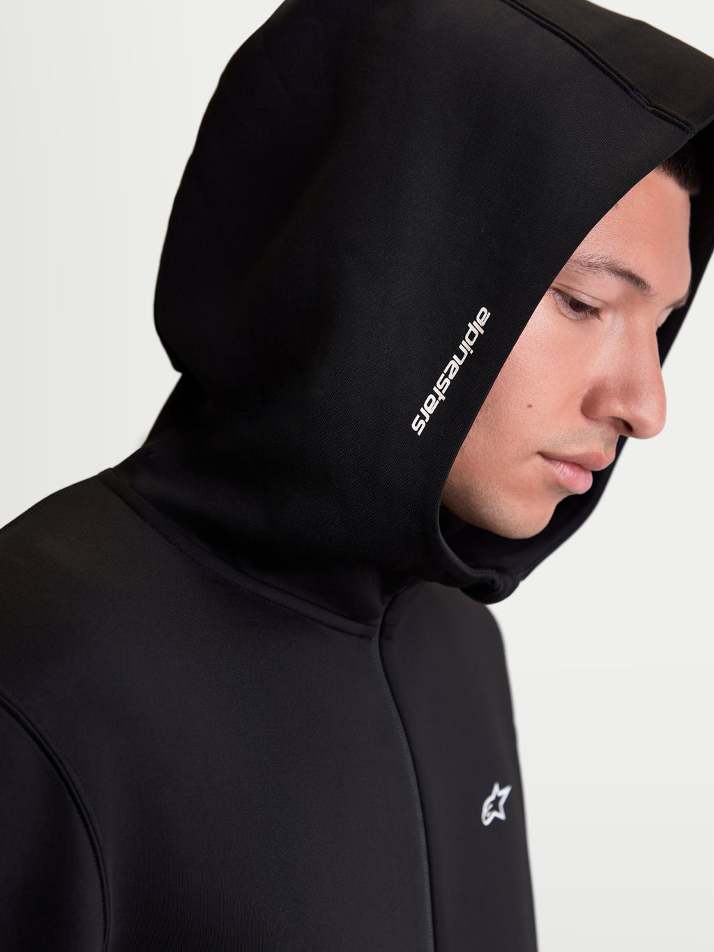 Alpinestars Cypher, sudadera con capucha de forro polar para hombre con cremallera, negra, primer plano de modelo con capucha de cuello alto, logotipo Alpinestars blanco y forro polar técnico de mezcla triple