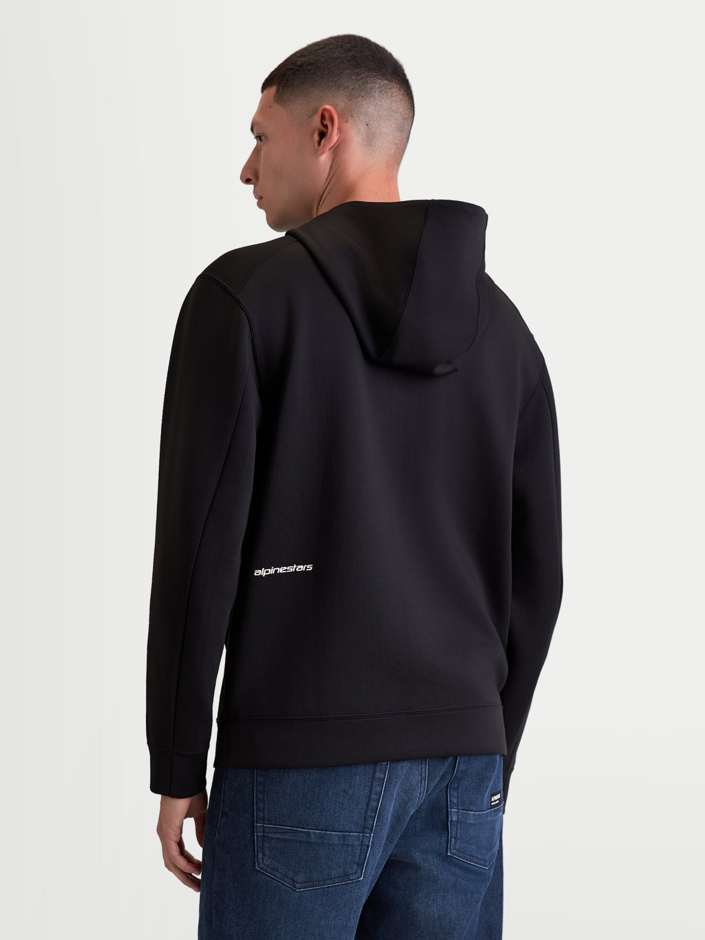 Alpinestars sudadera con capucha Cypher, sudadera deportiva de hombre con cremallera, negra, forro polar de doble cara de mezcla triple, vista posterior en modelo con capucha de cuello alto y logotipo de Alpinestars blanco en la parte inferior de la espalda