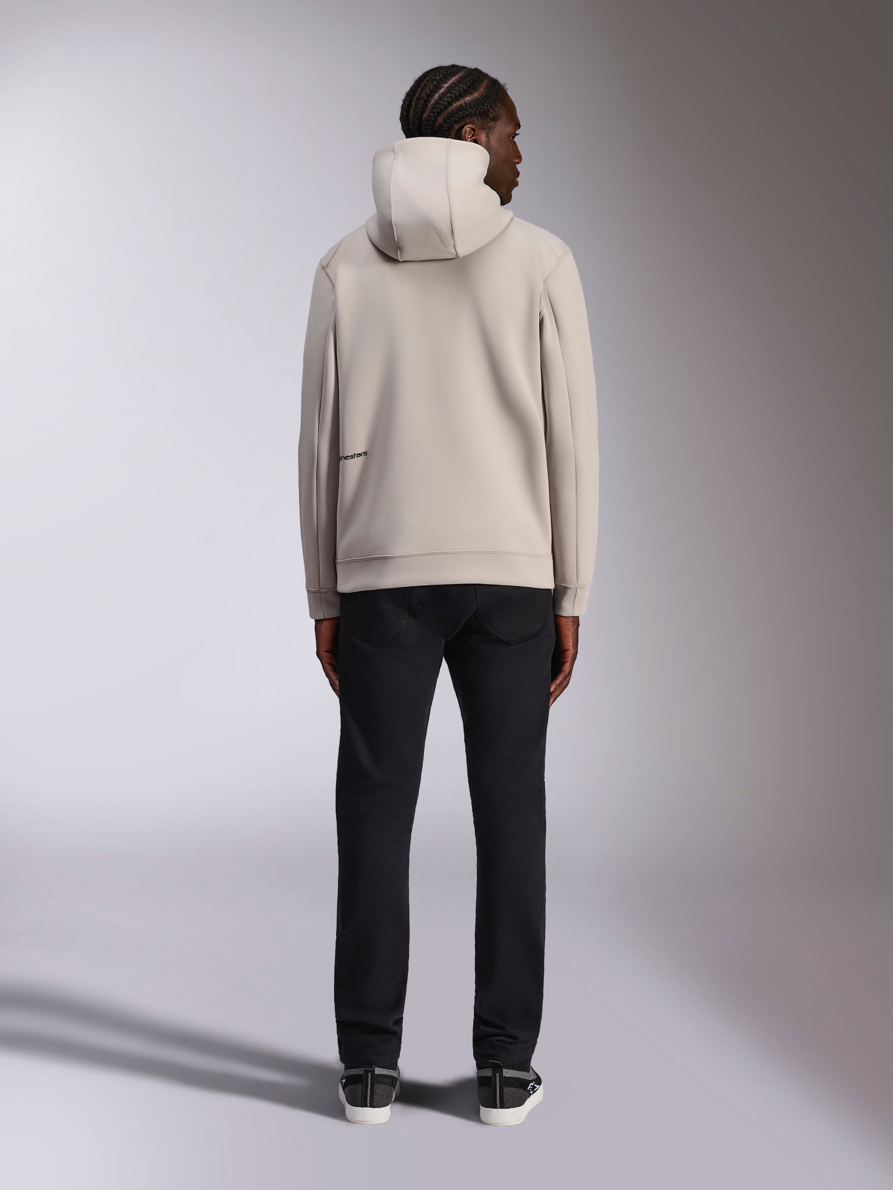 Alpinestars Cypher Hoodie, gris claro Cement, vista trasera de un hombre con sudadera de forro polar con cremallera completa, capucha de cuello alto y marca Alpinestars en la espalda, estilo urbano casual inspirado en el motociclismo combinado con pantalones negros