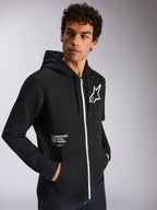 Alpinestars Transverse Hoodie, casual sportswear, black with white zipper detail, drawstring hood, Alpinestars star logo on chest, 'One Goal One Vision' graphic, worn by male model with dark curly hair