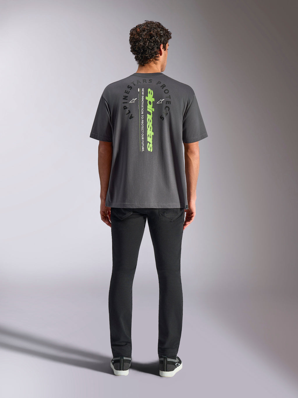 Camiseta Alpinestars Overhang Oversized CSF, de manga corta, gris carbón, vista posterior con logotipo vertical de Alpinestars en verde neón y texto gráfico, ajuste de gran tamaño, moda urbana informal de automovilismo