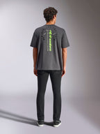 Camiseta Alpinestars Overhang Oversized CSF, de manga corta, gris carbón, vista posterior con logotipo vertical de Alpinestars en verde neón y texto gráfico, ajuste de gran tamaño, moda urbana informal de automovilismo