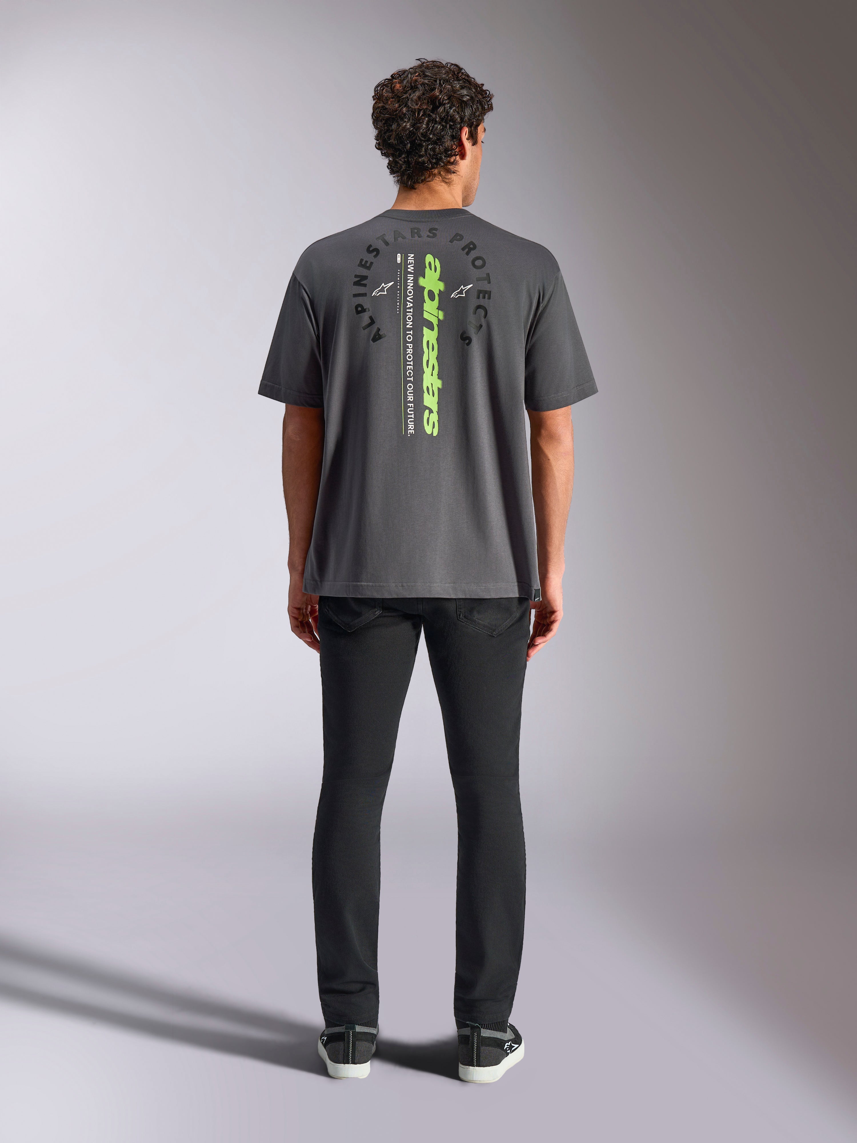 Camiseta Alpinestars Overhang Oversized CSF, de manga corta, gris carbón, vista posterior con logotipo vertical de Alpinestars en verde neón y texto gráfico, ajuste de gran tamaño, moda urbana informal de automovilismo