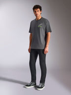 Alpinestars Overhang Oversized CSF Tee, camiseta de manga corta, gris carbón, con logotipo Astars blanco y texto verde en el pecho, modelo con pantalones negros y zapatillas, ajuste relajado oversized, ropa de calle casual de automovilismo
