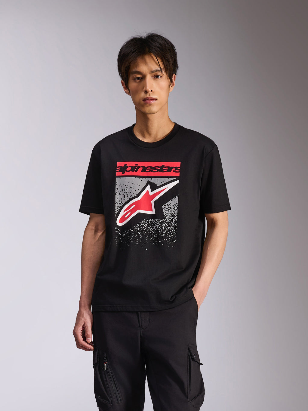 Camiseta Alpinestars Noka CSF, camiseta de manga corta, negra, con el texto Alpinestars en rojo y el logotipo Astars en rojo y blanco con un degradado MX moteado en gris, estilo streetwear casual inspirado en el motociclismo