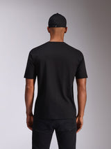 Alpinestars Ellipsoid CSF Tee, camiseta de manga corta, negra, vista trasera en modelo, combinada con una gorra negra y pantalones oscuros, ropa urbana casual inspirada en el automovilismo