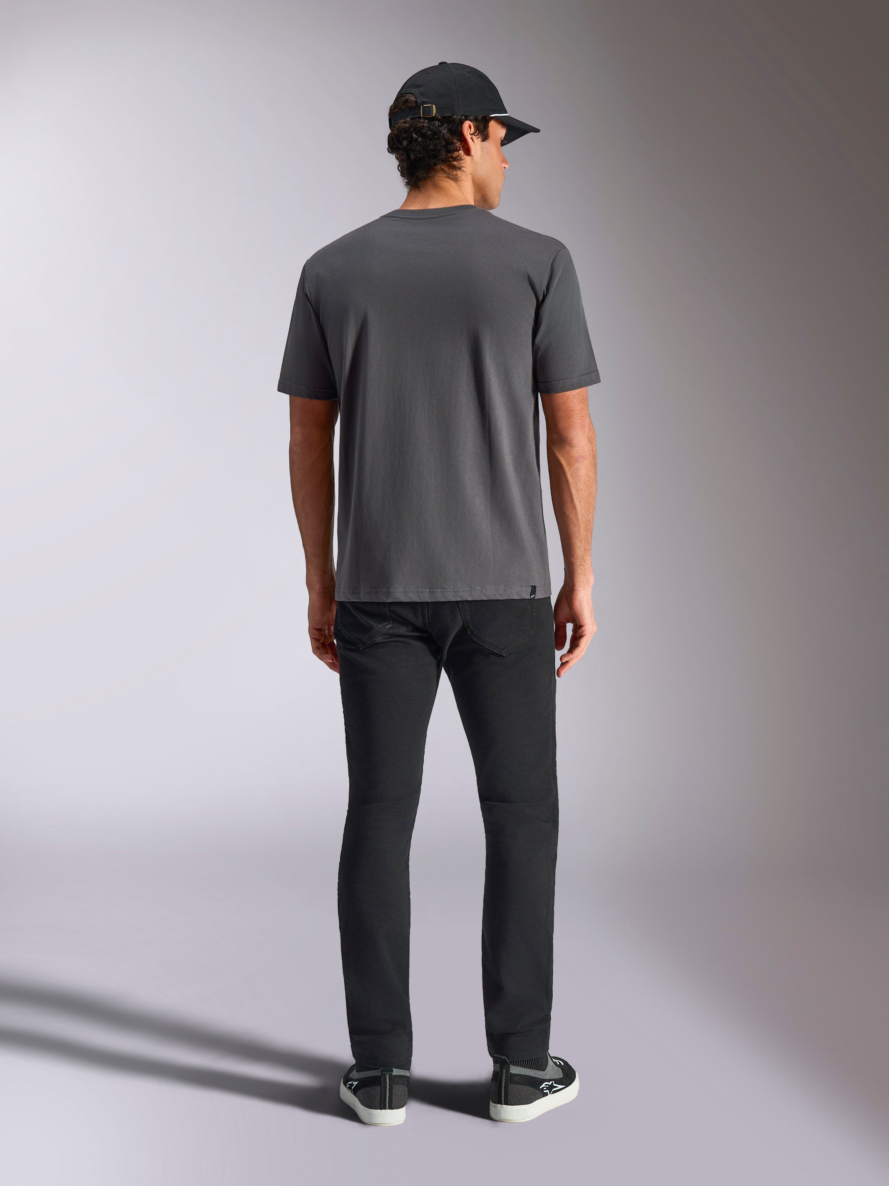Camiseta Alpinestars Ellipsoid CSF, camiseta de manga corta, gris carbón, vista posterior mostrada en modelo con gorra y pantalones negros, estilo urbano casual