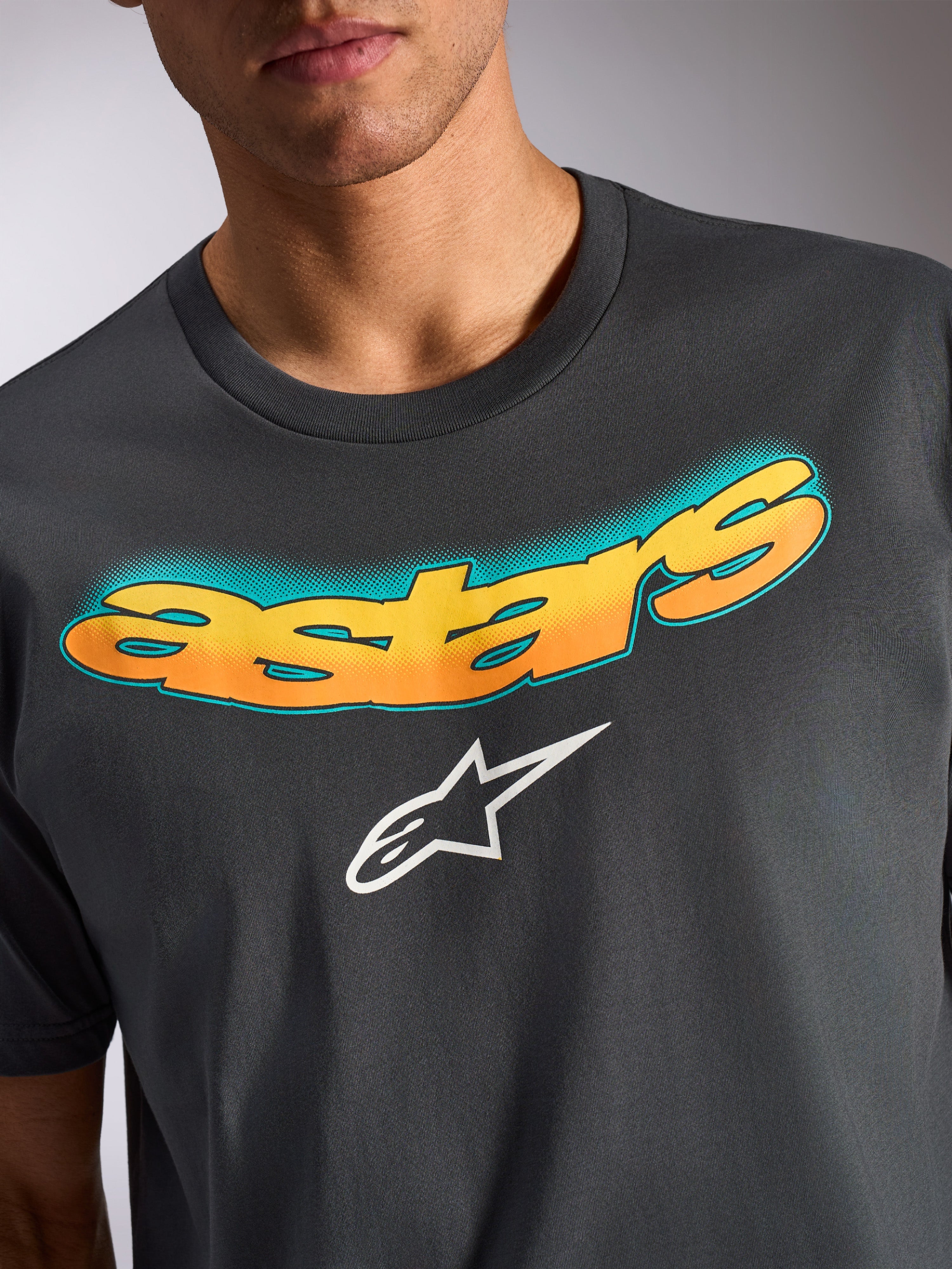 Camiseta Alpinestars Ellipsoid CSF, camiseta de manga corta, gris carbón, palabra 'astars' curvada con degradado amarillo y naranja y patrón de puntos verde azulado, logotipo de la estrella de Alpinestars en blanco, ropa casual inspirada en el automovilismo