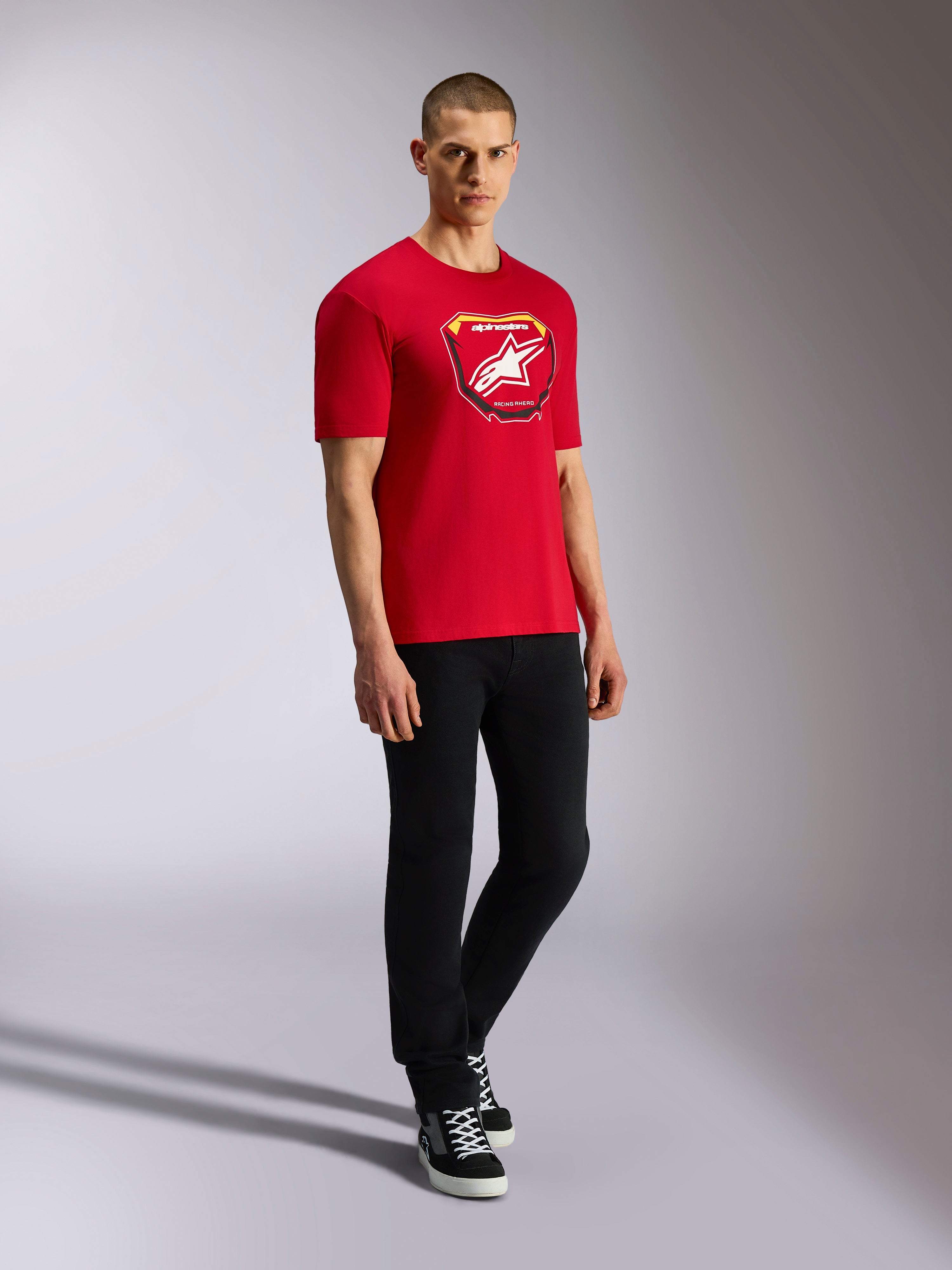 Alpinestars Plate CSF Tee, camiseta de manga corta, roja, gráfico frontal de placa Astars MX con logo de estrella blanca, usada por modelo con pantalones negros, estilo casual de moda urbana de automovilismo