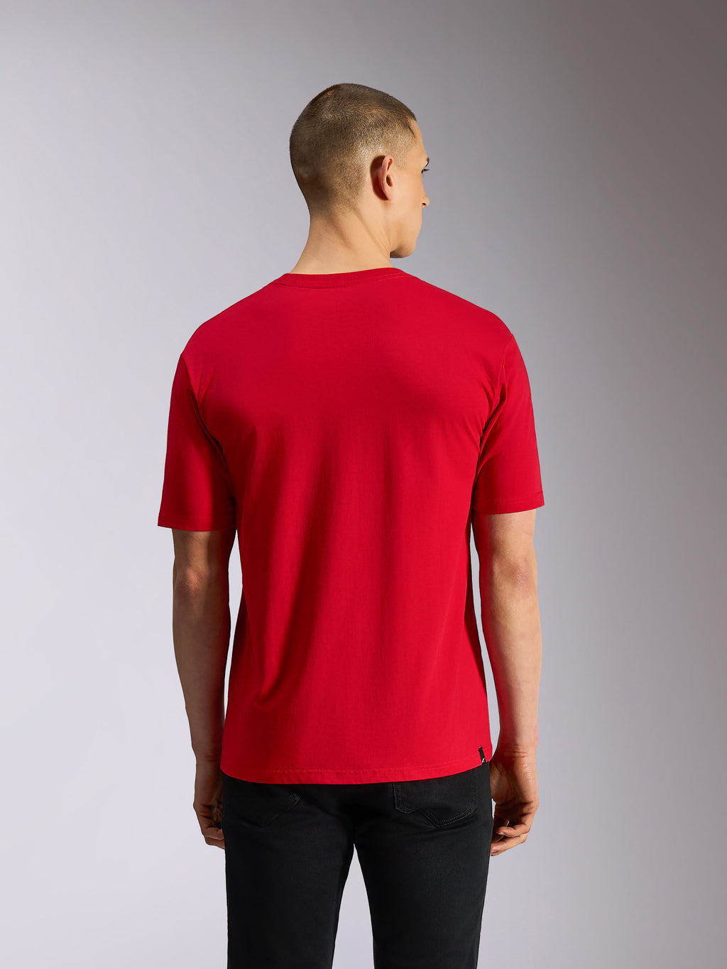 Alpinestars Plate CSF Tee, camiseta de manga corta, roja, vista posterior que muestra el tejido rojo liso y un ajuste casual, combinada con pantalones negros, streetwear inspirado en el motociclismo