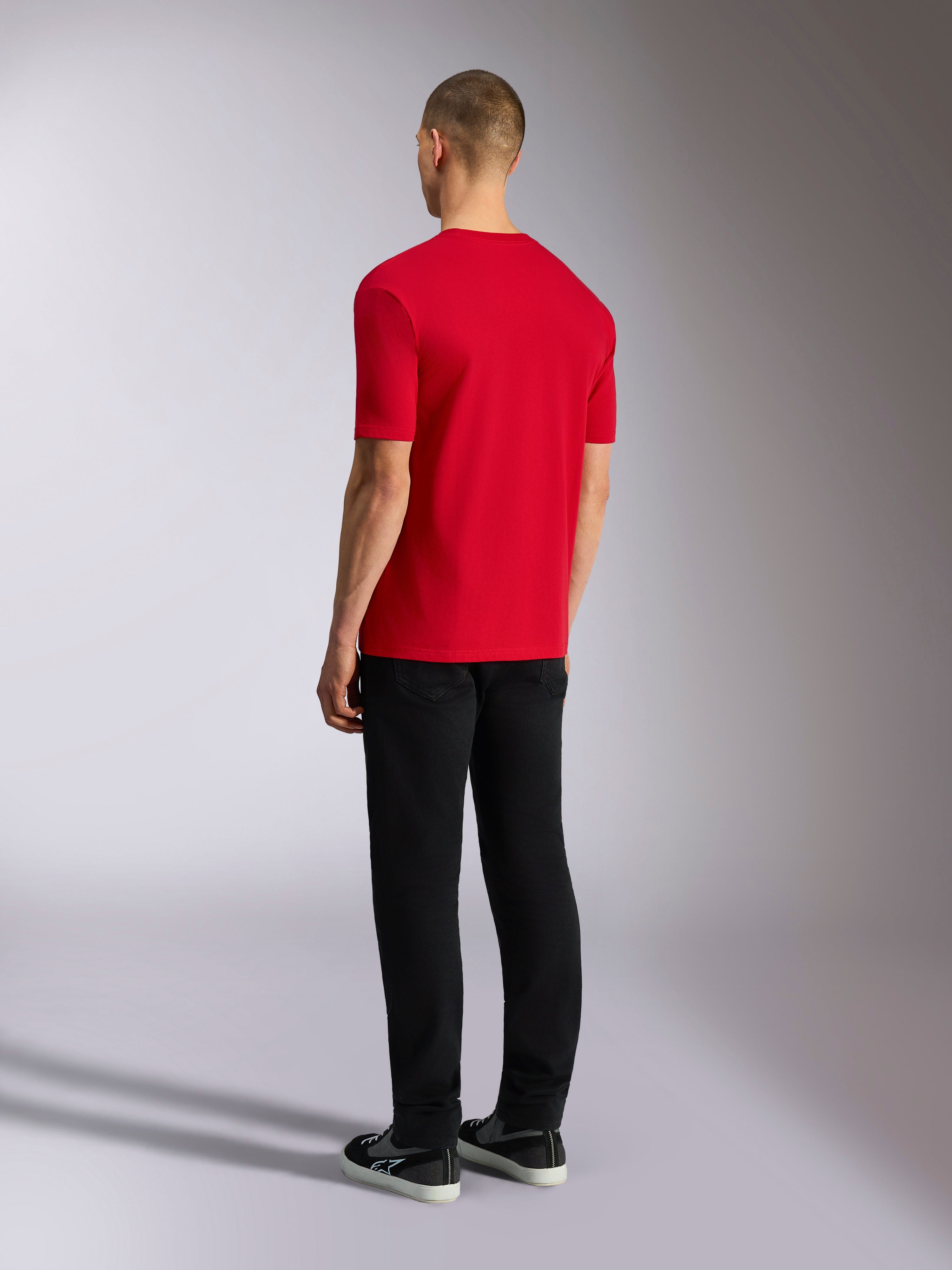 Alpinestars Plate CSF Tee, camiseta de manga corta, roja, vista posterior, usada con pantalones negros y zapatillas, ropa de calle casual inspirada en el automovilismo