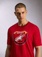 Camiseta Alpinestars Plate CSF, camiseta de manga corta, roja, con un gráfico frontal de placa de MX con el logotipo de Alpinestars y el texto 'Racing Ahead', usada por un modelo masculino, ropa deportiva casual inspirada en el automovilismo