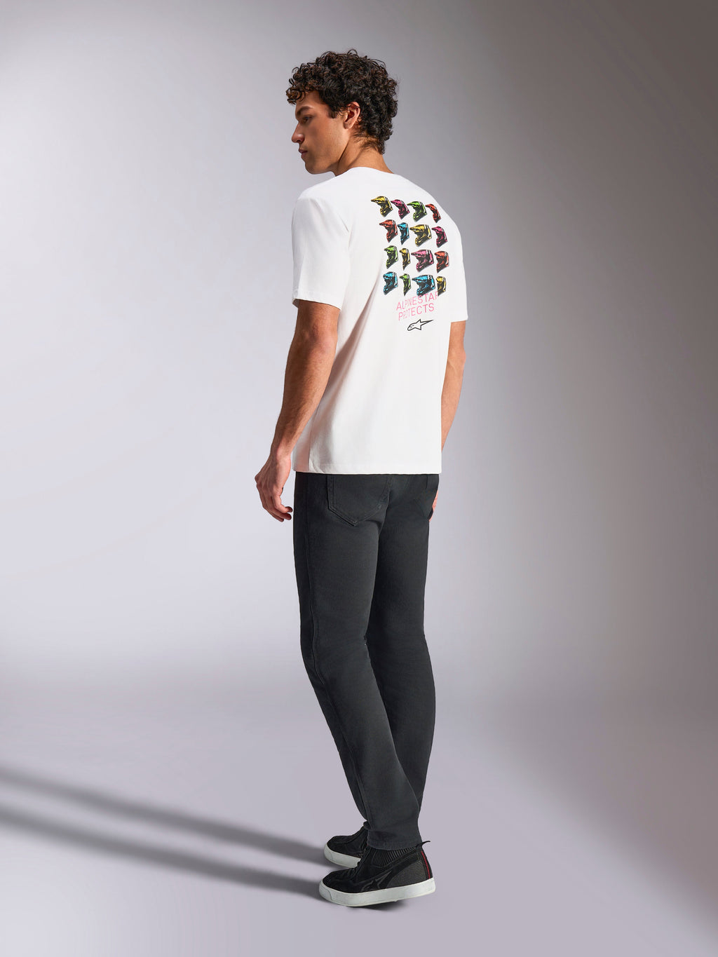 Alpinestars Pop Helmet CSF Tee, Short Sleeve T-Shirt, White, back view on model showing colorful M10 helmet graphic art, styled with dark pants and black sneakers, casual motorsport-inspired streetwear