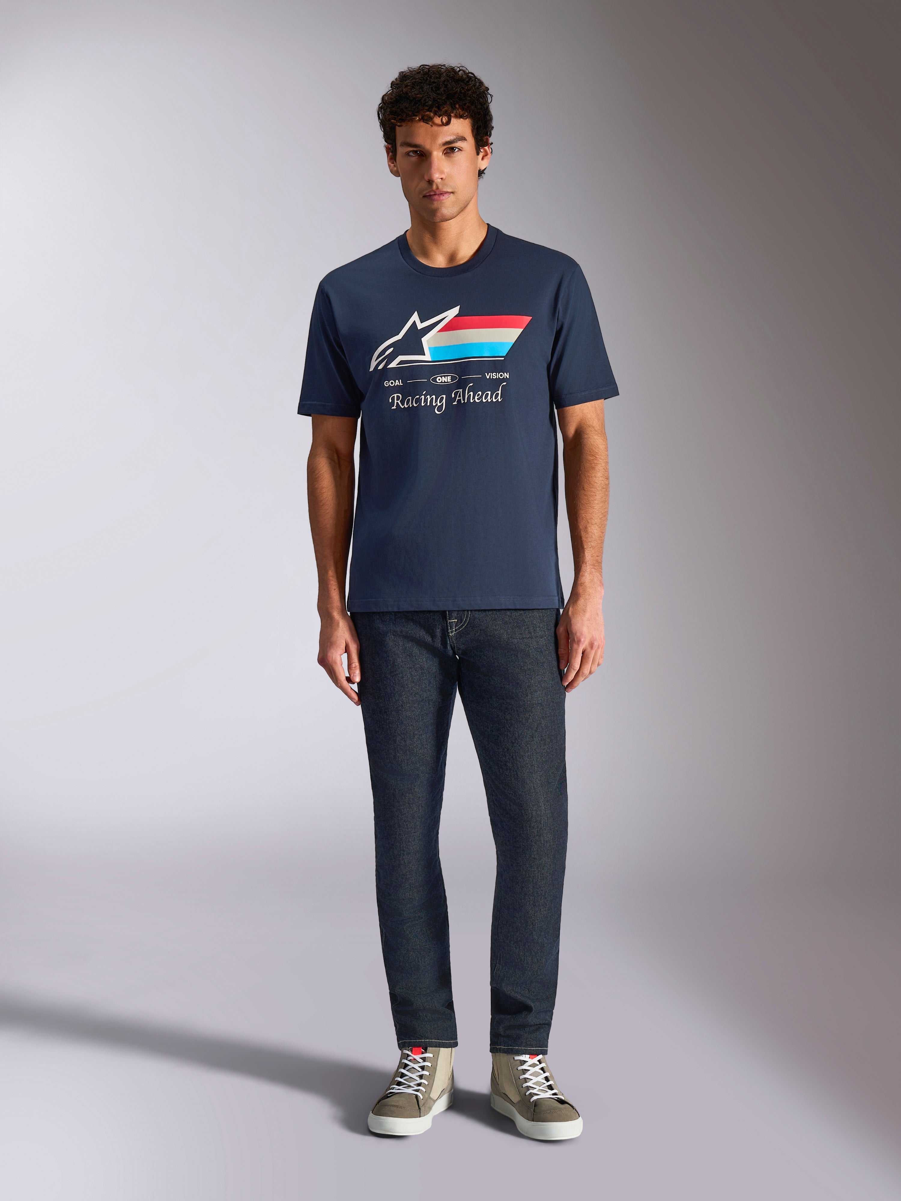 Alpinestars Trifecta CSF Tee, Short Sleeve T-Shirt, Navy Blue, White Astars Logo with Red White and Light Blue Stripes and 'Racing Ahead' text, worn with dark jeans and olive sneakers, Casual Motorsport Streetwear
