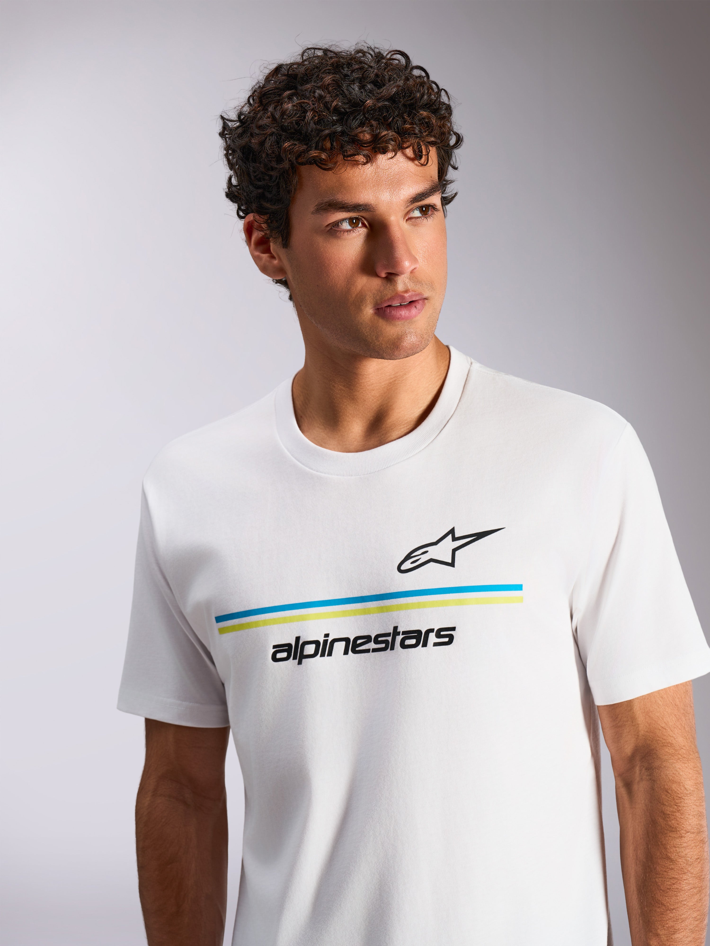 Alpinestars Lanes CSF Tee, camiseta de manga corta blanca con rayas horizontales en azul y verde lima, logotipo Astars y marca denominativa en negro, lucida por un modelo de cabello rizado, ropa de calle casual inspirada en el automovilismo
