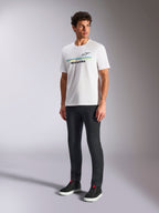 Camiseta Alpinestars Lanes CSF, camiseta blanca de manga corta, vestida por un modelo con pantalones negros ajustados y zapatillas altas negras, con rayas horizontales azules y amarillas y el logotipo de Alpinestars en el pecho, estilo urbano casual inspirado en el automovilismo