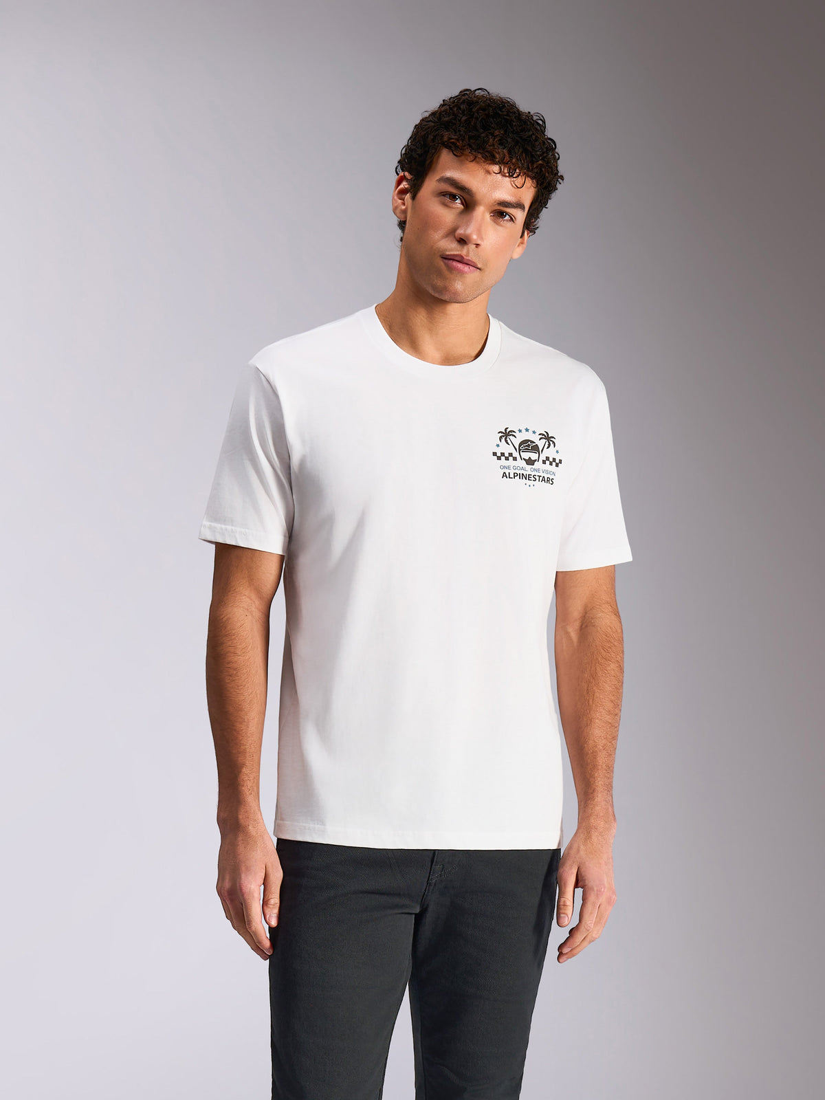 Alpinestars Order CSF Tee, camiseta de manga corta, blanca, gráfico en el pecho con casco y palmeras, usada por un modelo con pantalones oscuros, ropa urbana casual inspirada en el motor