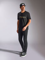 Camiseta Alpinestars Verdure Camo CSF, camiseta de manga corta, negra, con logotipo Astars con relleno de camuflaje en el pecho, lucida por un modelo con gorra y pantalones negros, estilo casual streetwear de motociclismo