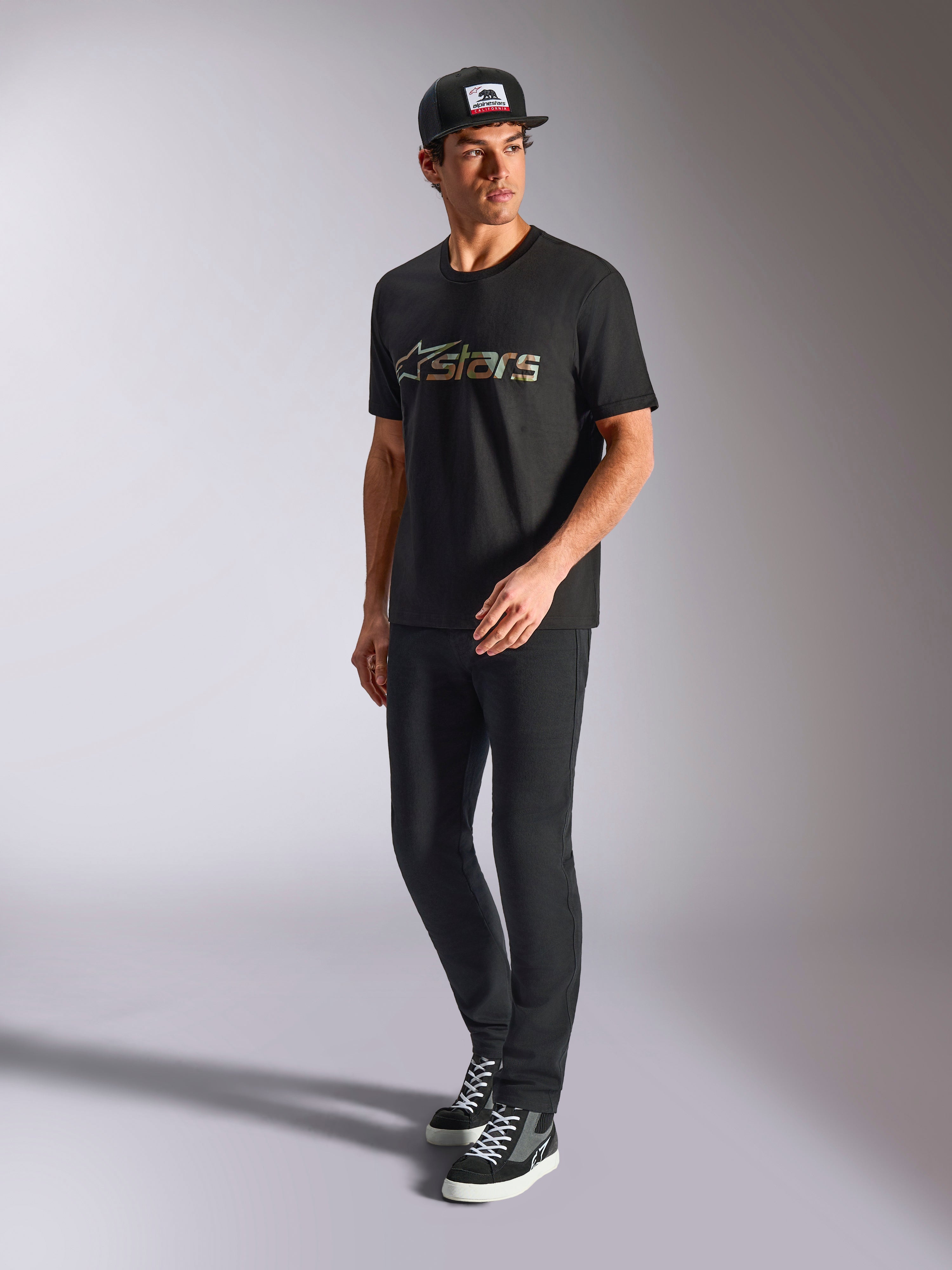 Camiseta Alpinestars Verdure Camo CSF, camiseta de manga corta, negra, con logotipo Astars con relleno de camuflaje en el pecho, lucida por un modelo con gorra y pantalones negros, estilo casual streetwear de motociclismo