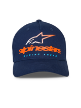 Gorra Alpinestars Instinct, gorra de béisbol azul marino, visera curva con corona estructurada, logotipo naranja de Alpinestars y logo de estrella a rayas en el frente, texto "RACING AHEAD" en azul claro, estilo deportivo casual