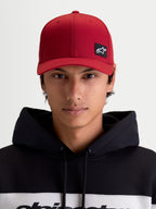 Alpinestars Gorra Pivot, gorra de béisbol estilo sportswear unisex, rojo oscuro, vista frontal en modelo con parche del logotipo Astars bordado, visera curva, corona estructurada y tejido de sarga resistente