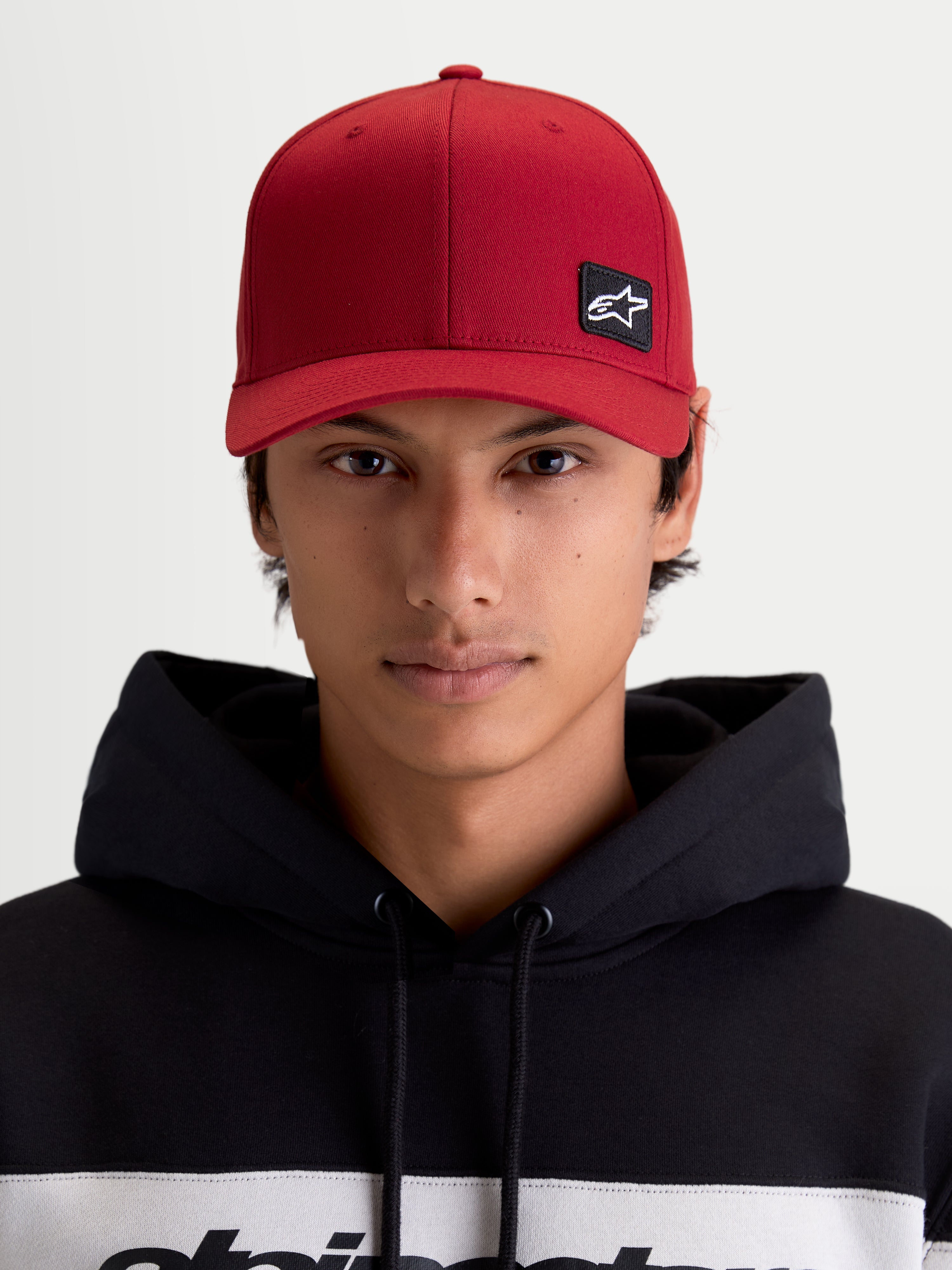Alpinestars Gorra Pivot, gorra de béisbol estilo sportswear unisex, rojo oscuro, vista frontal en modelo con parche del logotipo Astars bordado, visera curva, corona estructurada y tejido de sarga resistente