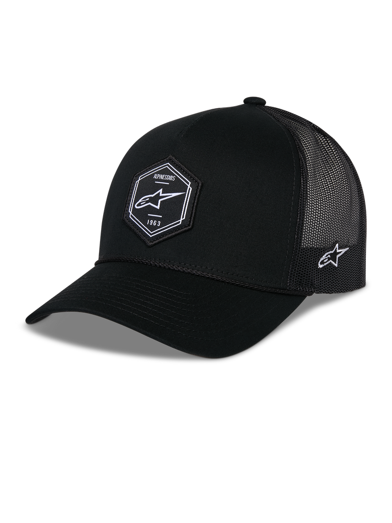 Gorra Alpinestars Hexeon Trucker, negra, cuenta con una corona estructurada con visera curva, parche tejido hexagonal en la parte frontal con logotipo de Astars en blanco y texto 1963, paneles traseros de malla de poliéster transpirable con bordado lateral del logotipo, accesorio de estilo casual inspirado en el automovilismo