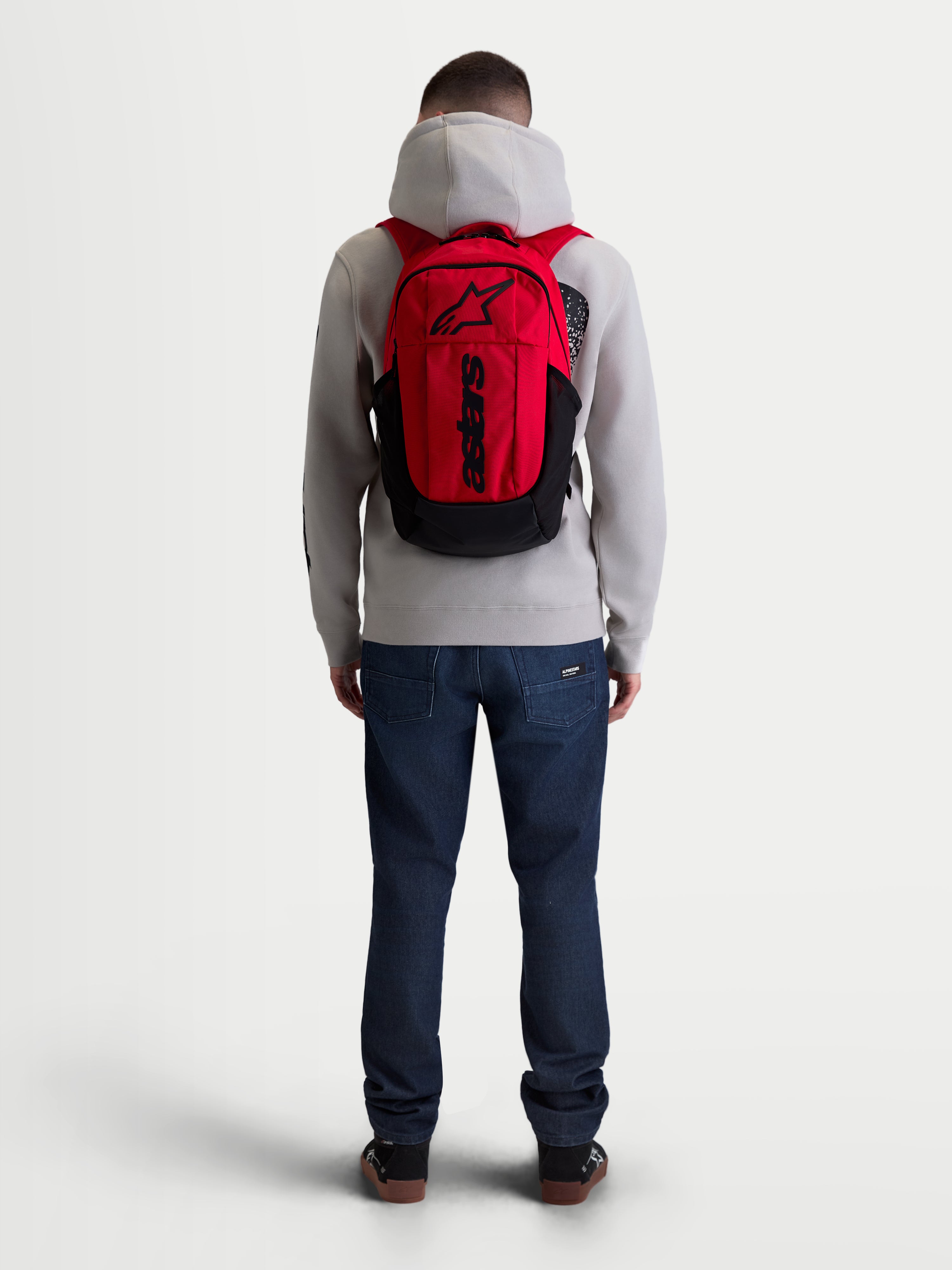 Alpinestars Mochila GFX Boss, mochila de estilo deportivo urbano de 20L, roja y negra, vista trasera en modelo, construcción de poliéster 600D duradero, funda interna para laptop y correas acolchadas con marca de silicona en relieve.