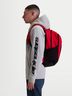 Alpinestars Mochila GFX Boss, mochila deportiva de 20 l, roja y negra, fabricada en poliéster 600D con bolsillos laterales de malla y correas acolchadas, mostrada en modelo para uso diario y urbano.