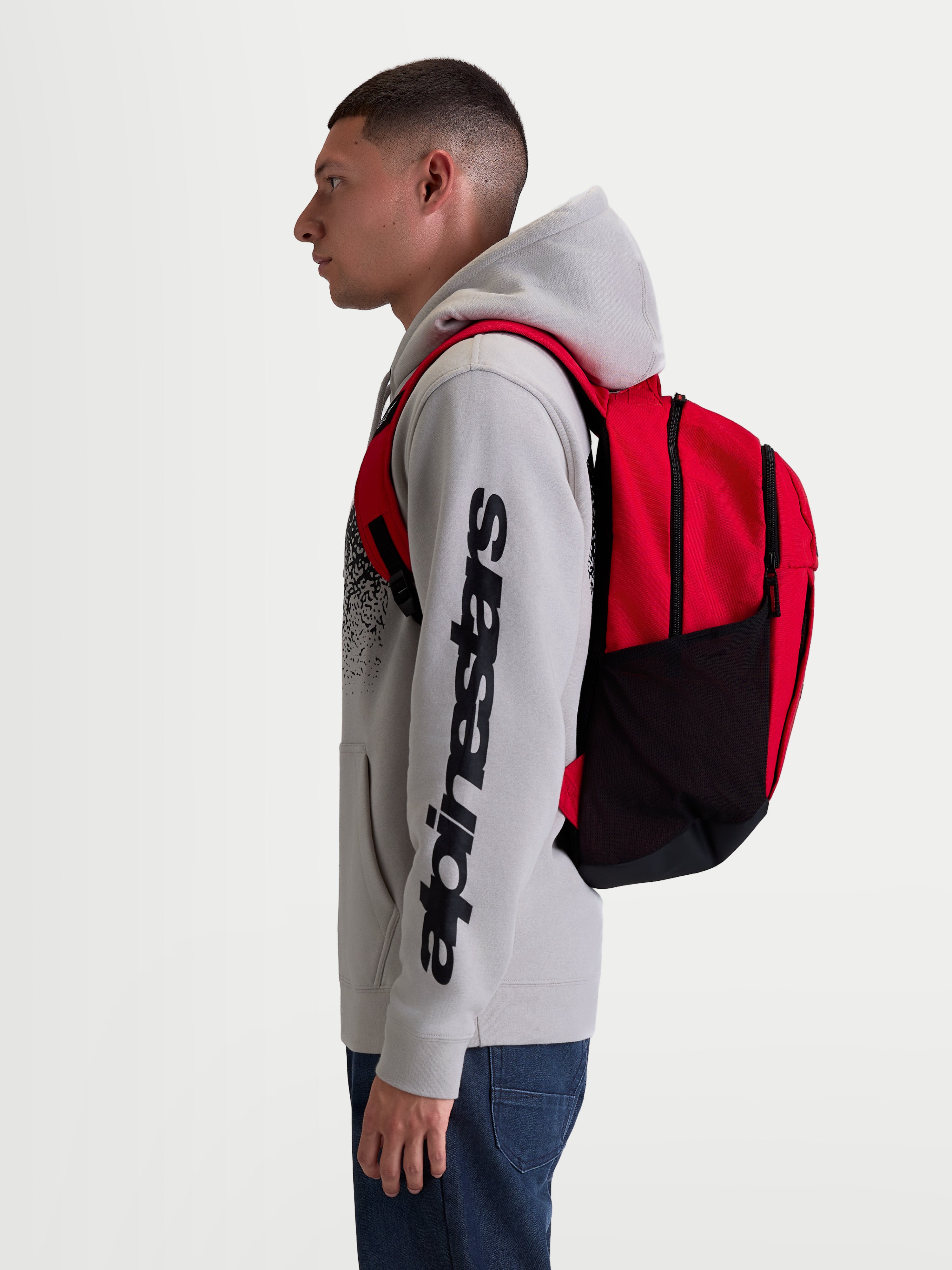 Alpinestars Mochila GFX Boss, mochila deportiva de 20 l, roja y negra, fabricada en poliéster 600D con bolsillos laterales de malla y correas acolchadas, mostrada en modelo para uso diario y urbano.