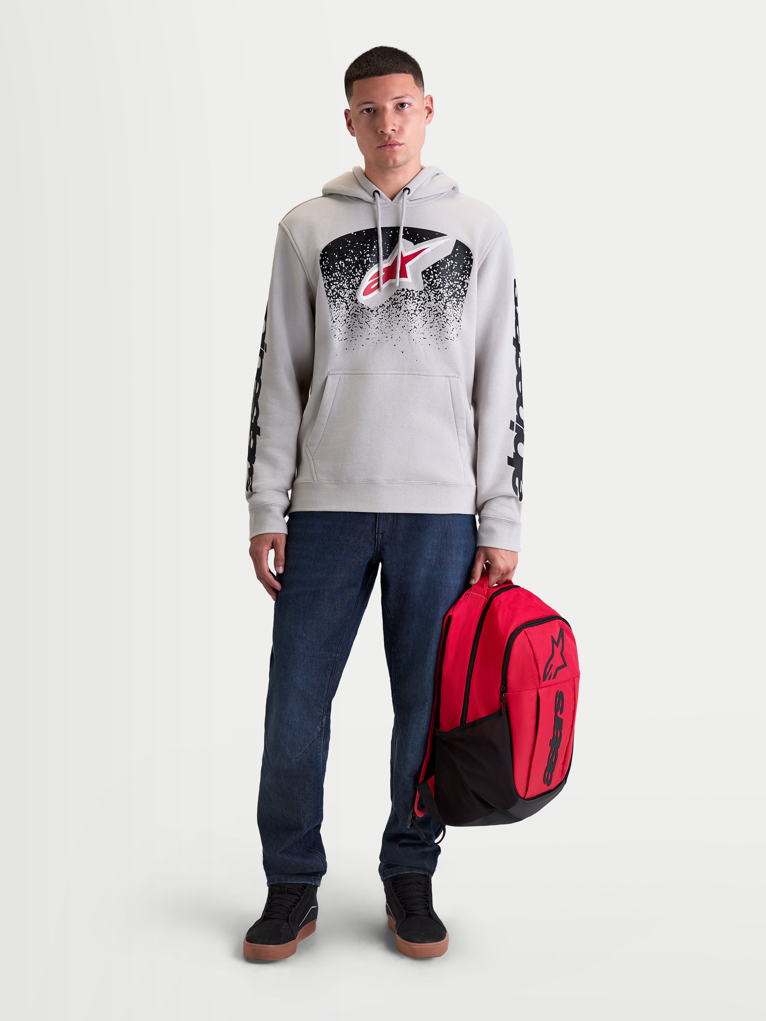 Alpinestars Mochila GFX Boss, mochila de deporte para hombre, roja y negra, capacidad de 20L, confeccionada en poliéster 600D duradero con logotipo Astars de silicona en relieve, modelo posando con la mochila para uso urbano casual