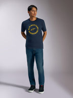 Alpinestars MX CSF Tee, Short Sleeve T-Shirt, Navy Blue, featuring a yellow circular Alpinestars Motocross graphic, worn by a model with blue jeans and black sneakers, casual motorsport streetwear