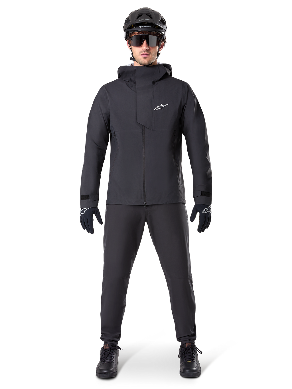 Chaqueta impermeable Alpinestars A-Dura Elite, negra, combinada con pantalones y guantes de ciclismo a juego, casco negro y gafas de sol, con el logotipo de Astars en blanco en el pecho, diseño técnico de alto rendimiento para ciclismo de montaña