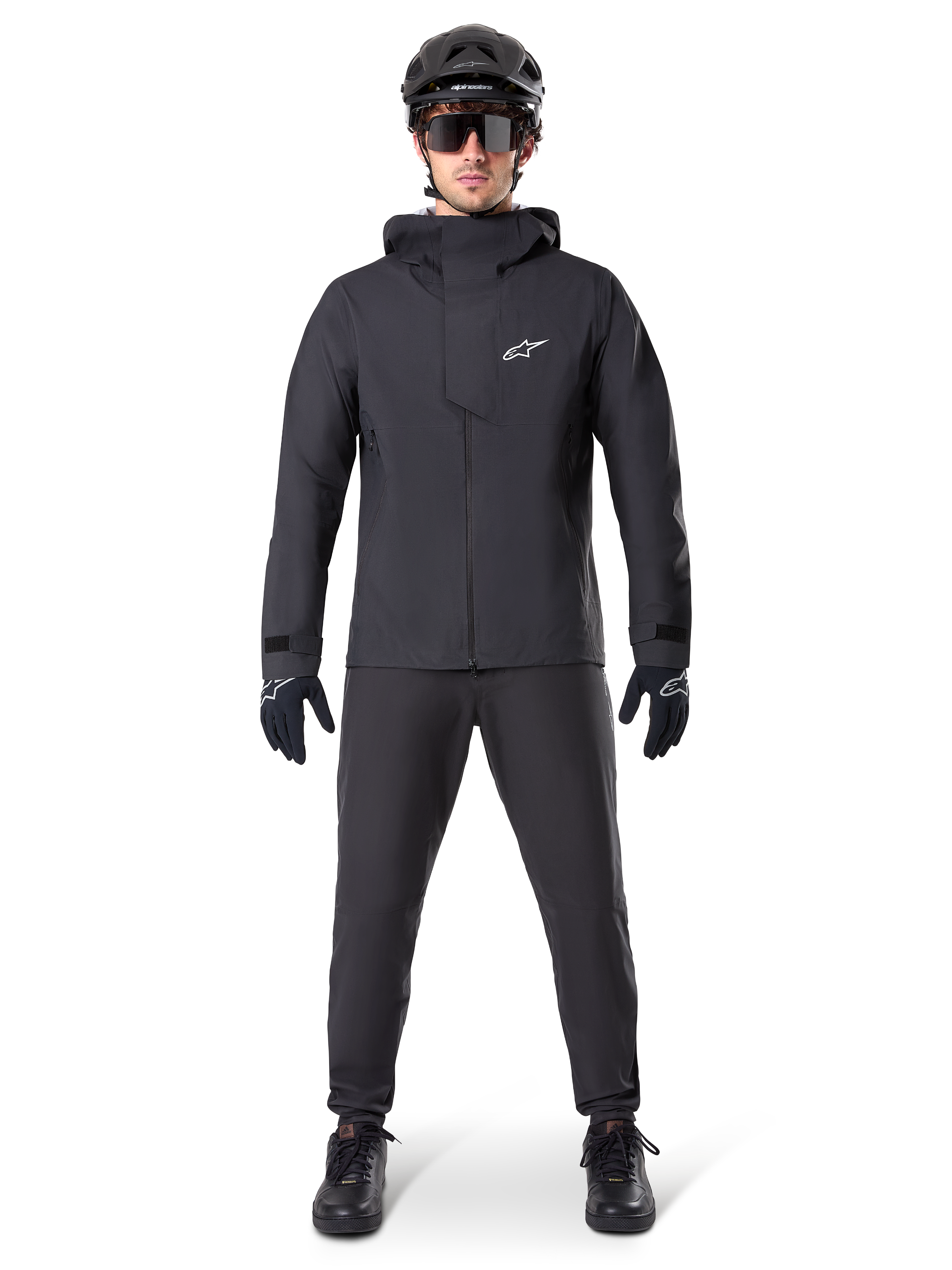 Chaqueta impermeable Alpinestars A-Dura Elite, negra, combinada con pantalones y guantes de ciclismo a juego, casco negro y gafas de sol, con el logotipo de Astars en blanco en el pecho, diseño técnico de alto rendimiento para ciclismo de montaña