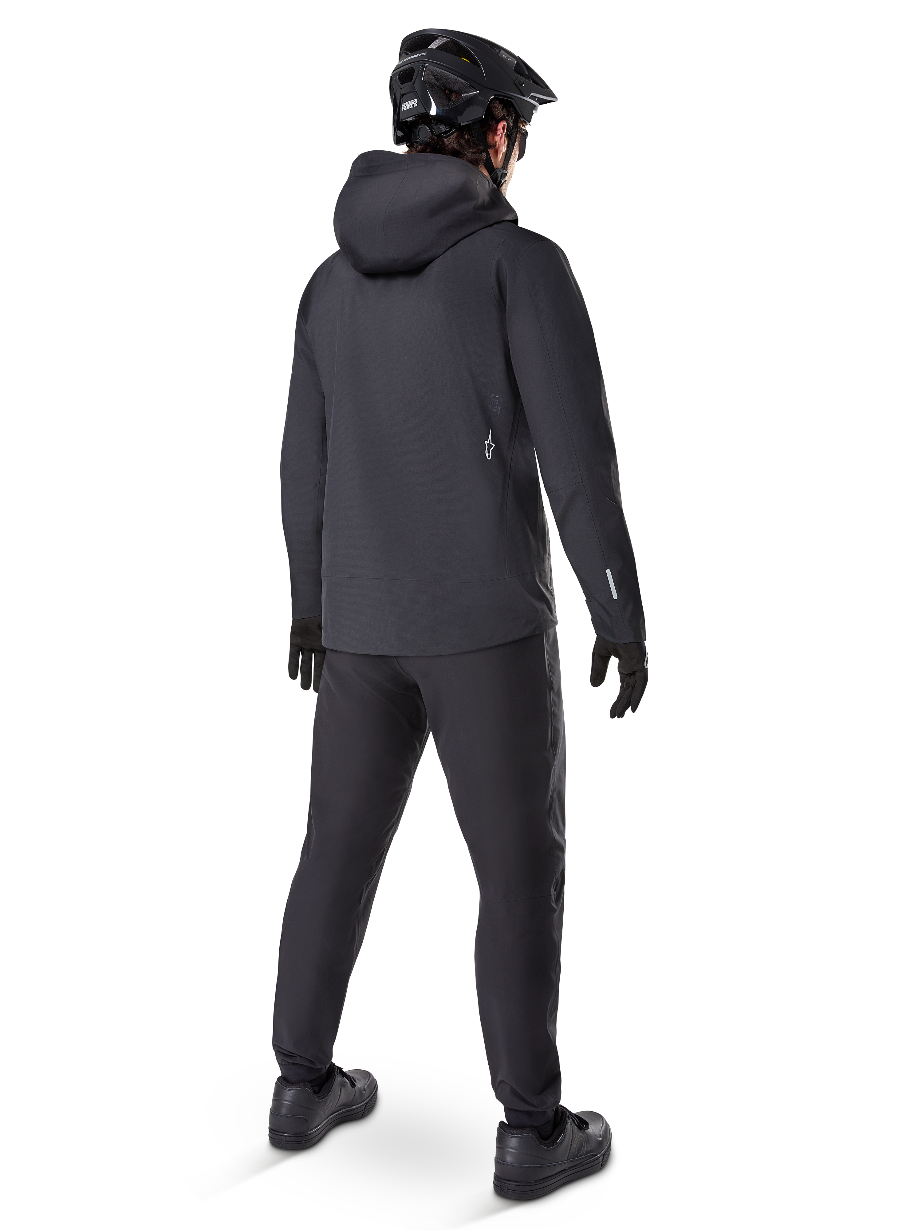 Chaqueta Impermeable Alpinestars A-Dura Elite, color negro, vista trasera que muestra la capucha compatible con el casco y el dobladillo trasero más largo, combinada con pantalones de MTB, guantes y casco negros a juego para una protección completa en senderos bajo cualquier condición climática.