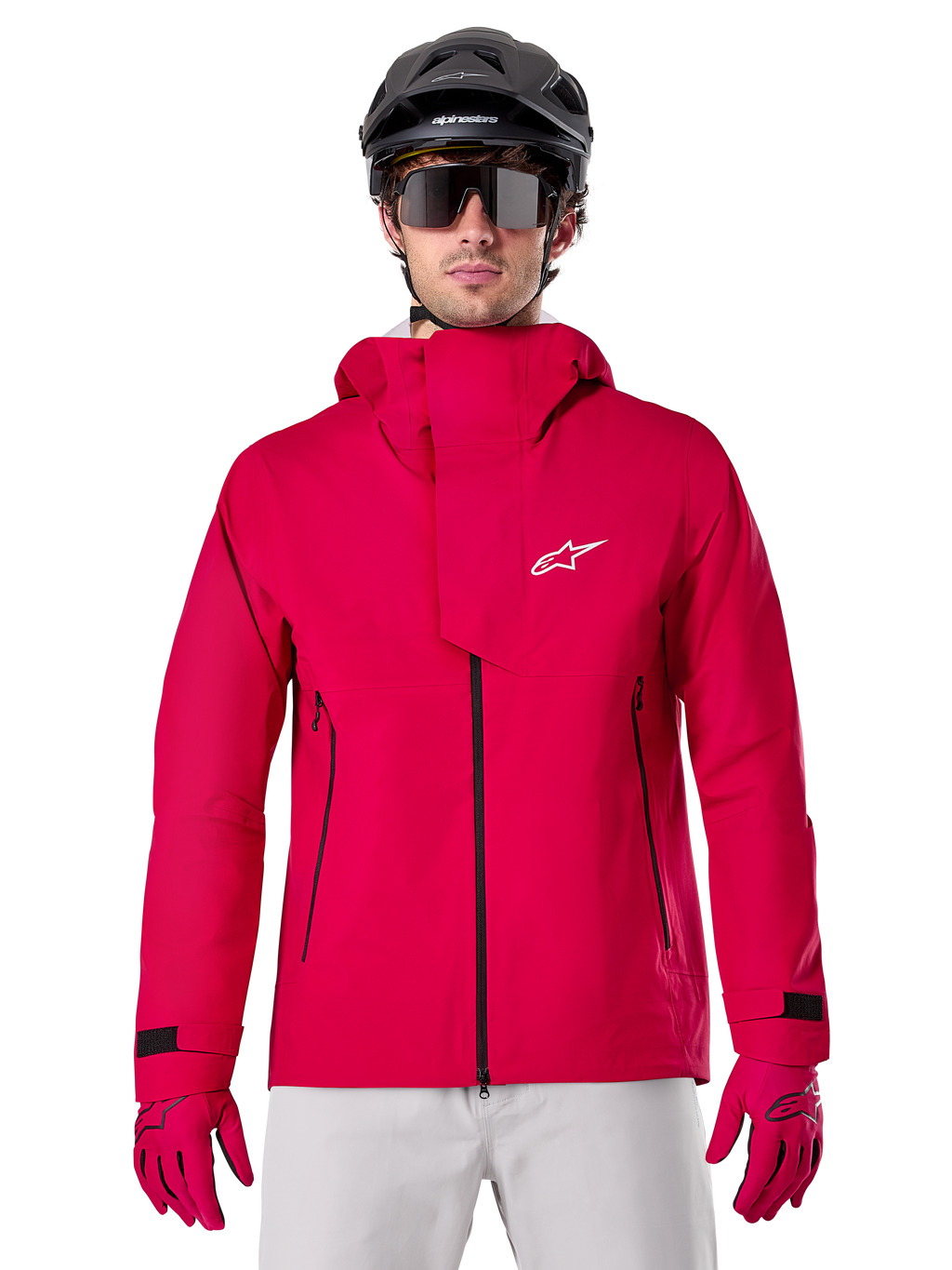 Alpinestars A-Dura Elite Waterproof Jacket, chaqueta de lluvia para MTB, rojo flúor, cuello alto con logotipo de Alpinestars en blanco, detalles de cremalleras negras, usada con guantes a juego y casco de ciclismo negro, equipamiento técnico impermeable