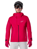 Alpinestars A-Dura Elite Waterproof Jacket, chaqueta de lluvia para MTB, rojo flúor, cuello alto con logotipo de Alpinestars en blanco, detalles de cremalleras negras, usada con guantes a juego y casco de ciclismo negro, equipamiento técnico impermeable
