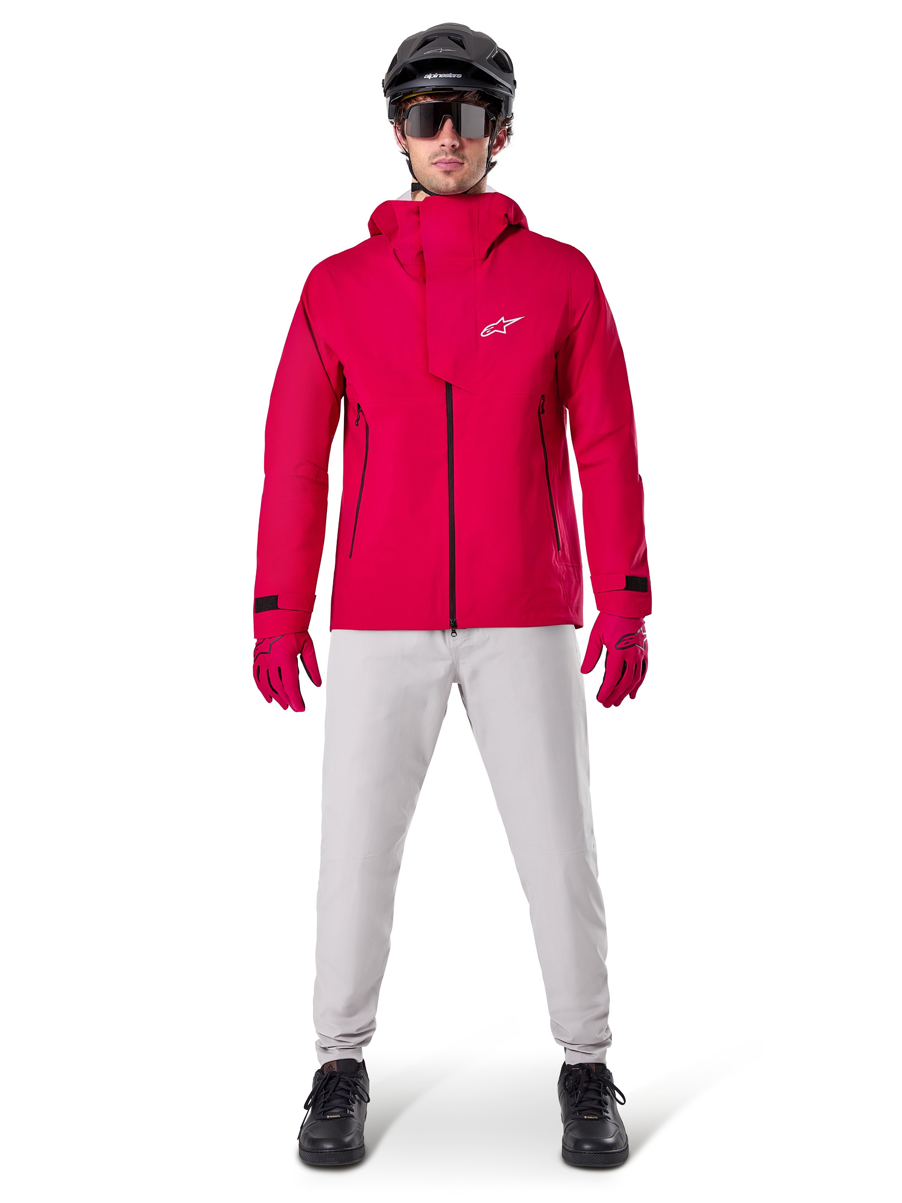 Chaqueta impermeable Alpinestars A-Dura Elite, Rojo Fluo, chaqueta técnica de montaña usada con un casco negro de MTB, gafas de sol, guantes rojos a juego y pantalones gris claro, vista de cuerpo completo del equipamiento de ciclismo para todo tipo de clima