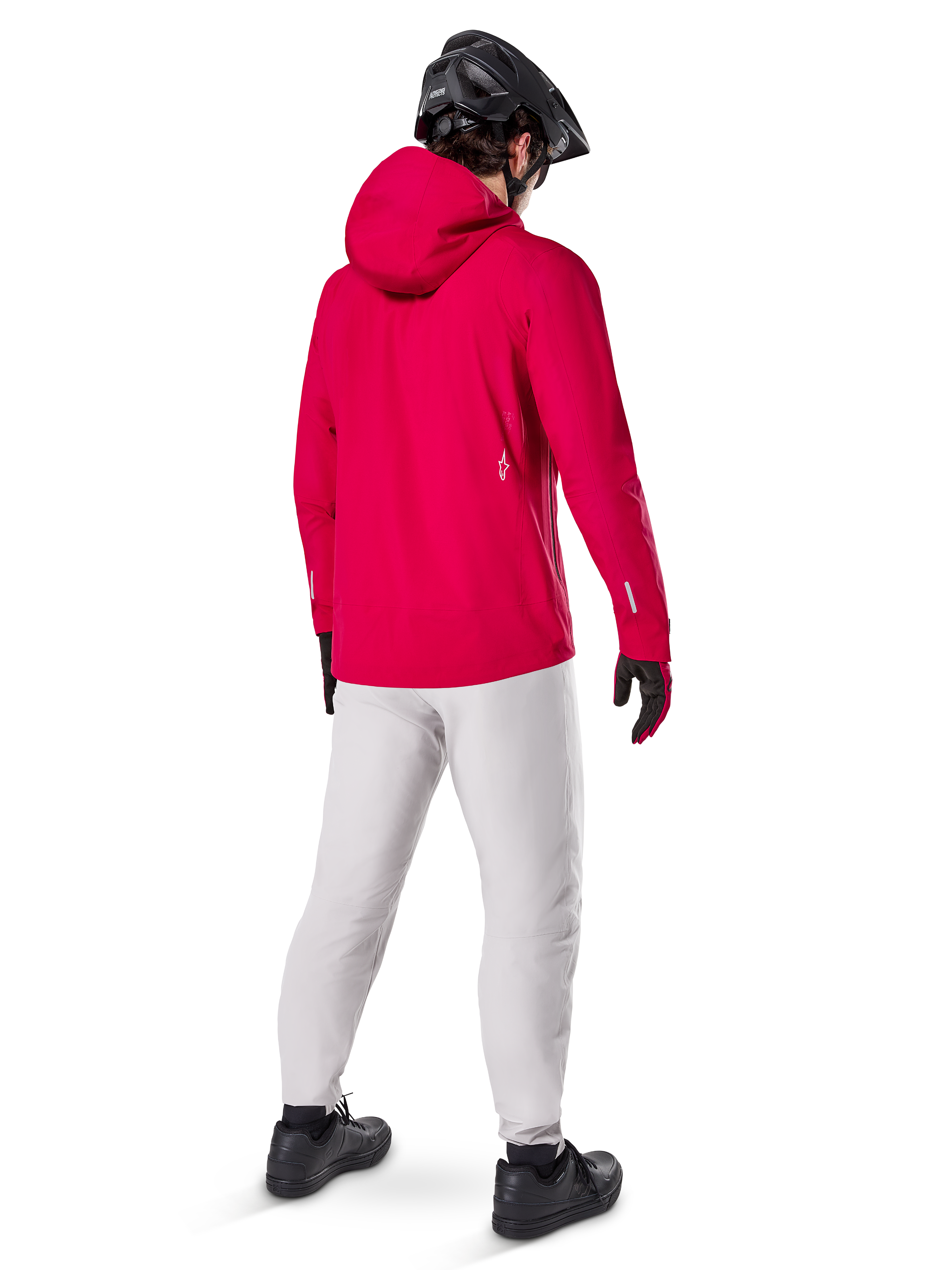 Alpinestars A-Dura Elite, chaqueta impermeable, Rojo Fluo, vista trasera de tres cuartos, combinada con pantalones gris claro y casco de MTB negro, cuenta con capucha y detalles reflectantes, chaqueta de lluvia de alto rendimiento para ciclismo de montaña