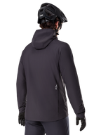 Alpinestars A-Dura Thermal Jacket, negra, vista trasera, usada con un casco de bicicleta de montaña negro y guantes, cuenta con un pequeño logo blanco de Astars en la parte baja de la espalda, chaqueta de ciclismo ligera con aislamiento térmico