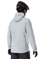 Chaqueta térmica Alpinestars A-Dura, Gris Titanium, vista posterior de un ciclista con la chaqueta aislante con capucha, combinada con un casco de MTB negro y guantes negros, con un pequeño logotipo de Alpinestars en la parte inferior de la espalda, diseñada para ciclismo de montaña en climas fríos.