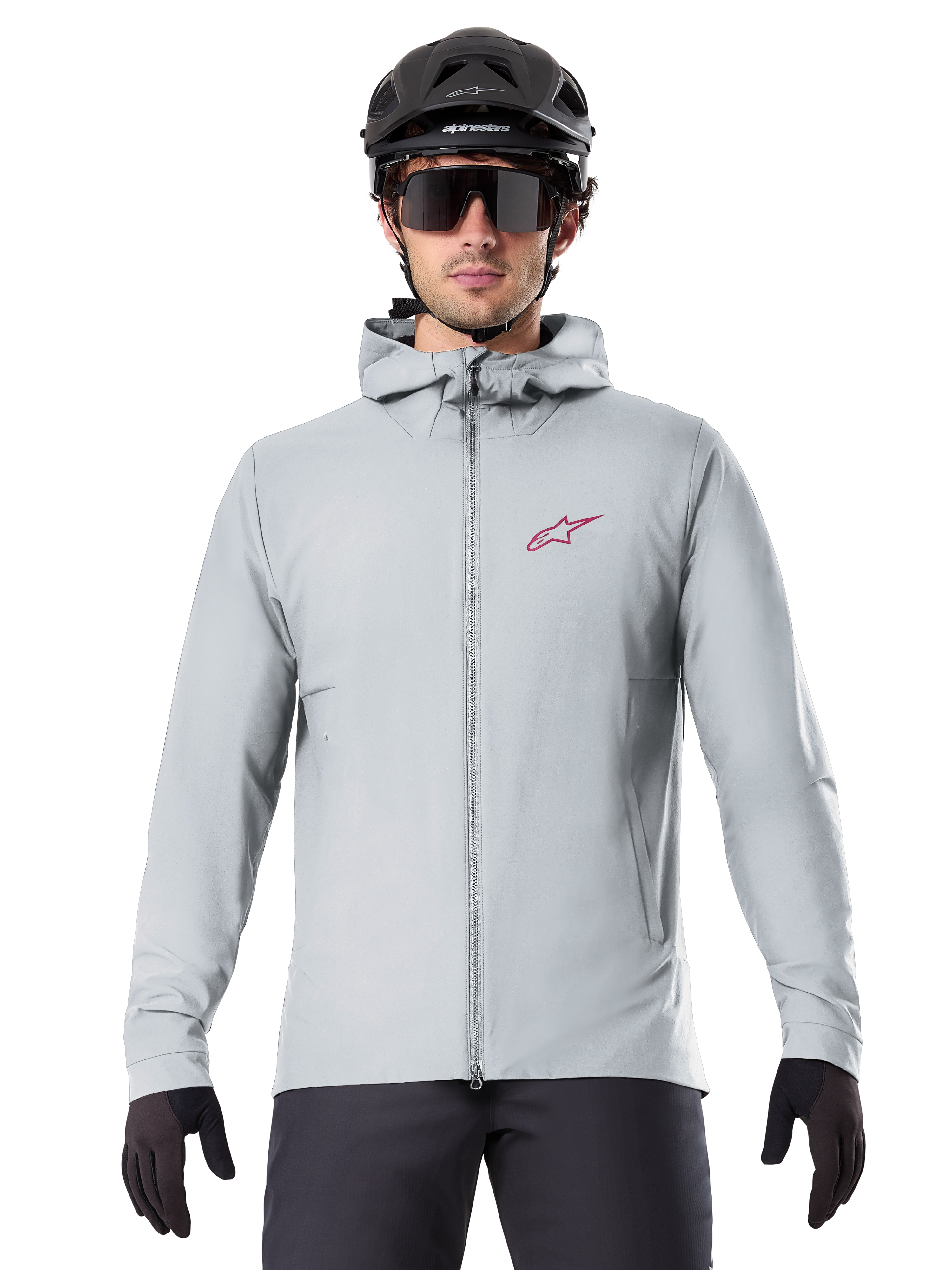 Chaqueta térmica Alpinestars A-Dura en color Titanium, chaqueta de ciclismo con capucha en gris claro con un logotipo de estrella roja en el pecho, usada por un ciclista con casco de MTB negro, gafas de sol y guantes, equipamiento aislante para ciclismo de montaña